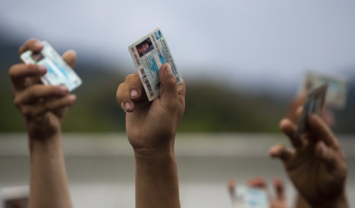 Migrants hold up their Honduran national ID cards as Guatemalan police block their passage at the Honduras-Guatemala border.