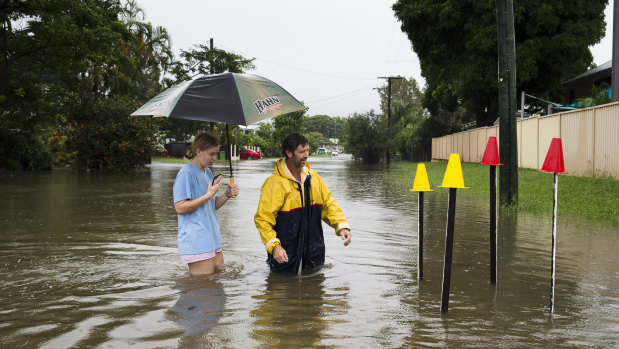 Local resident Paul Shafer and daughter Lily standing in floodwaters in Hermit Park, Townsville, on Saturday. Paul has been opening storm water drains near his house to reduce flooding, with the star pickets showing where the storm water cover has been removed. 
