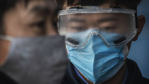 A Chinese railway worker has fogged safety goggles as he waits to check the temperature of arriving passengers a train station in Beijing.