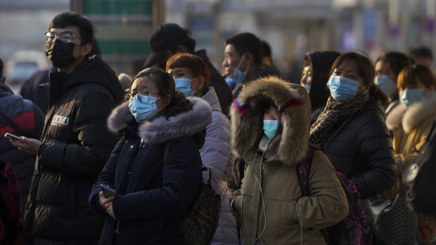 Commuters wearing face masks to help curb the spread of the coronavirus wait for buses at a bus stand in Beijing.