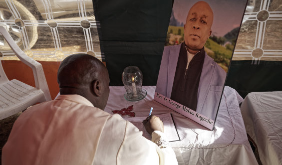 Father Michael Wa Mugi lights a candle and signs the book of condolence next to a photo of Catholic priest Reverend George Mukua Kageche, who died in the Ethiopian Airlines plane crash.
