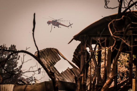 A helicopter with a water hose flies over a house destroyed by bushfires near the town of Bilpin.