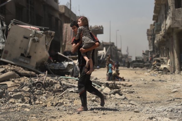 A young man runs barefoot carrying his sister as they escape from West Mosul.