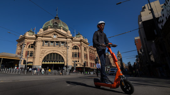 A man rides an e-scooter past Flinders Street Station.