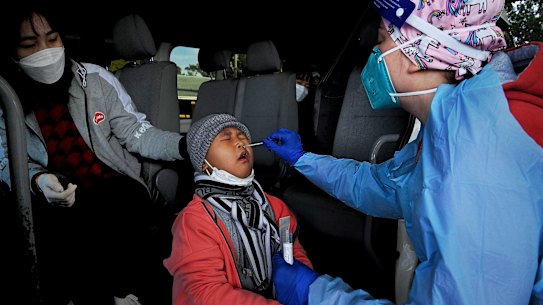 SydPath nurse Petra Vieco gives Chhorng Nty, 8, a COVID-19 test, watched by his sister Sivmey Nty, 15, at the Fairfield Showgrounds on Monday.