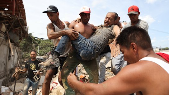 ベネズエラのラグアイラで地震が発生し、倒壊した建物の瓦礫の中から男性を運び出す近所の人たち。