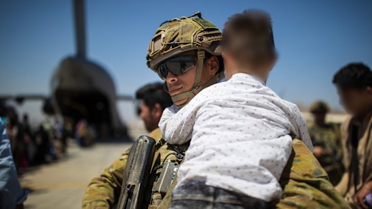 An Australian Army soldier carries an Afghan child while assisting a family aboard the RAAF C-17A Globemaster at the Hamid Karzai International Airport. 