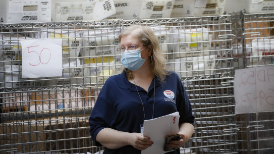 Cages loaded with ballots in United Postal Service bins rest behind a worker at a Board of Elections facility in New York.
