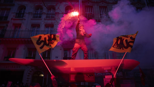 A member of the SUD Union stands on top of a bus shelter waving a flare as over 400,000 people took to the streets of Paris in protest as part of a nationwide strike against President Macron’s Pension reform plans.