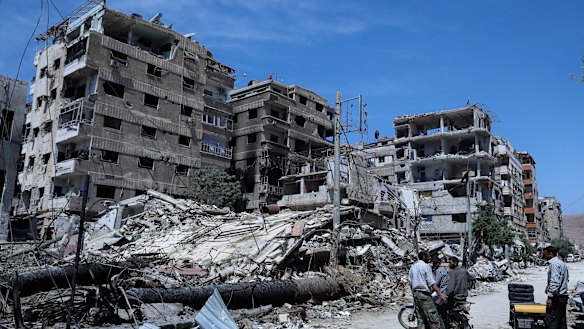 People stand in front of damaged buildings in the town of Douma a week after the April 2018 attack.