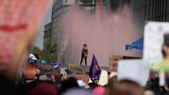 A woman stands on the ledge of a water fountain that has been stained red during a march for International Women's Day in Mexico City.