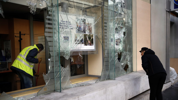 A worker clears debris in a bank as a man watches through smashed windows in Paris on Sunday.