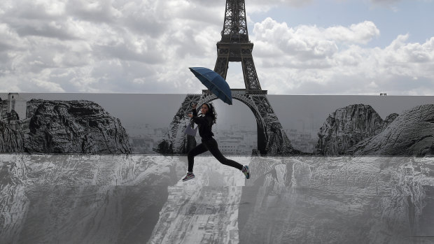 Culture in the air: a woman jumps in front of the Eiffel Tower where an exhibit has been installed. French President Emmanuel Macron is offering cash to stimulate young people’s consumption of art, music, and even video games.
