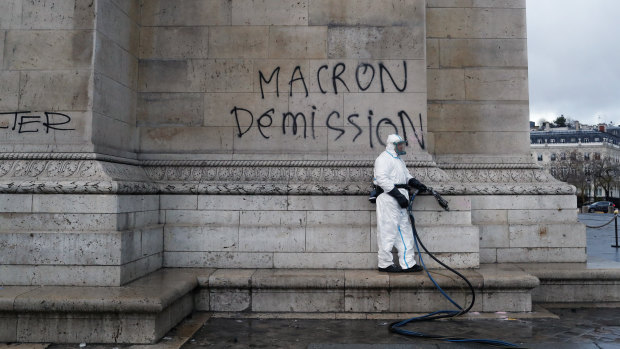 A worker about to clean graffiti saying " Macron resignation" on the Arc de Triomphe.