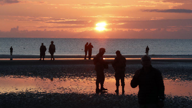 World War II reenactors gather at dawn on Omaha Beach in Normandy.