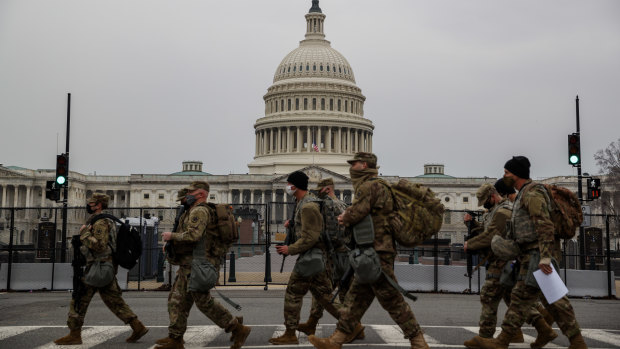National Guard troops walk past the US Capitol building on the first day of hearings to impeach Donald Trump.