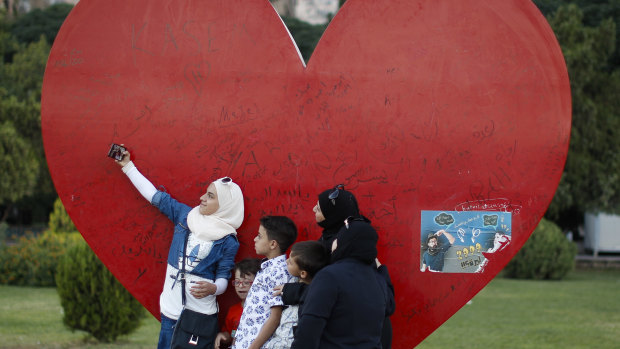 A Syrian girl uses her mobile phone to take a selfie with her family backdropped by a heart shape depicting love for Damascus, at Omayyid Square, Syria, on Tuesday. 