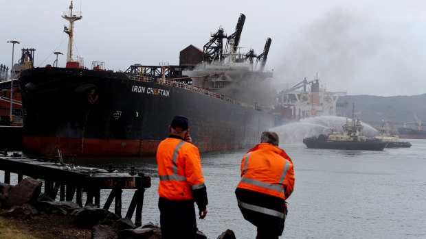 Onlookers watch as tugboats spray water onto the ship in an effort to cool it down.