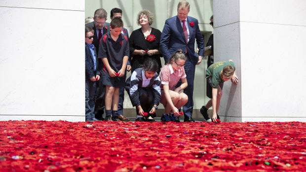 Senator Scott Ryan's son Nick Ryan, Aiden Makem, 10, from Tarcutta Public, Aysha Sajid, 11, from The Grange school in Minto, Annabell Wakefield, 12, from Uranquinty Public near Wagga, and Clay Barton, 11, from Kapooka Public add poppies to the poppy display in the Parliament House forecourt on Friday