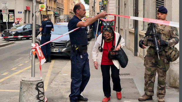 A police officer lets an elderly woman leave the area near the bomb site.