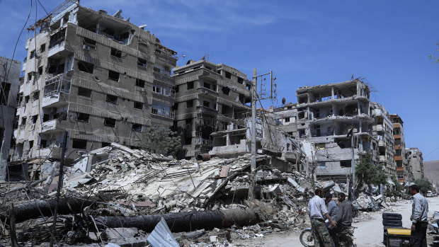 People stand in front of damaged buildings in the town of Douma a week after the April 2018 attack.