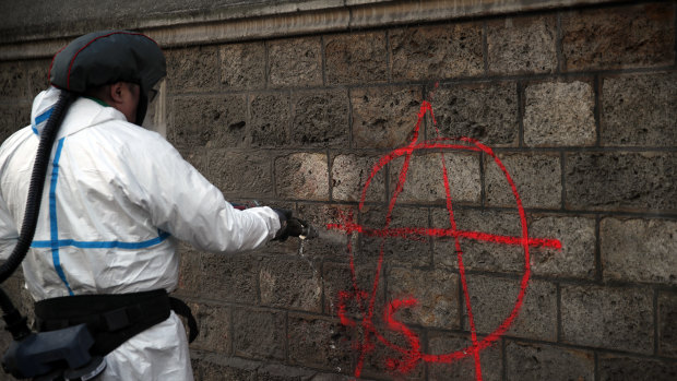 A municipal worker removes graffiti in Paris as monuments reopened, council workers cleaned debris and shop owners tried to put the city back together on Sunday.