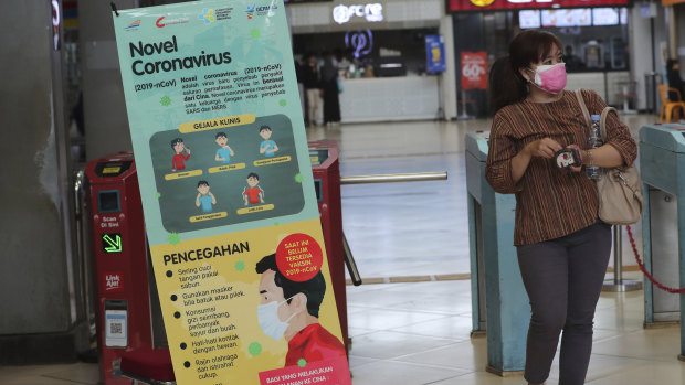 A woman passes an information banner on coronavirus at a train station in Jakarta, Indonesia. 