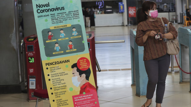 A woman wears a protective face mask as she passes an information banner on coronavirus at a train station in Jakarta, Indonesia. 