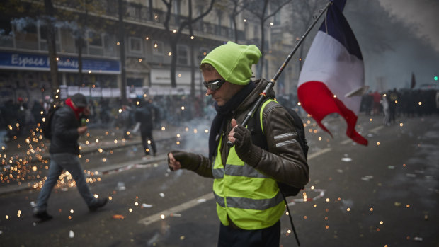 A Gilet Jaune, or Yellow Vest, holds a French Tricolor amidst tear gas as protesters and French Riot Police clash during a rally near Place de Republique on Thursday.