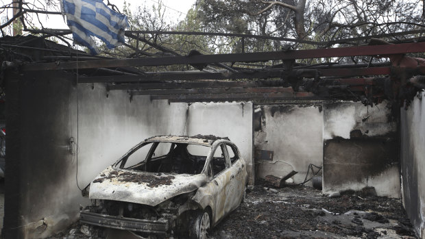 A Greek national flag flutters over the charred remains of a burned-out car and house in Mati.