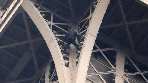 A climber is pictured between two iron columns of the Eiffel Tower.