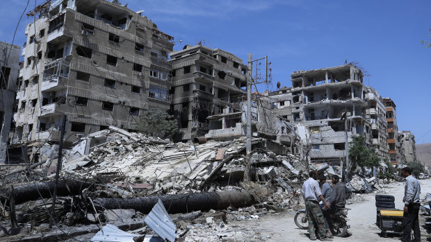 People stand in front of damaged buildings, in the town of Douma.