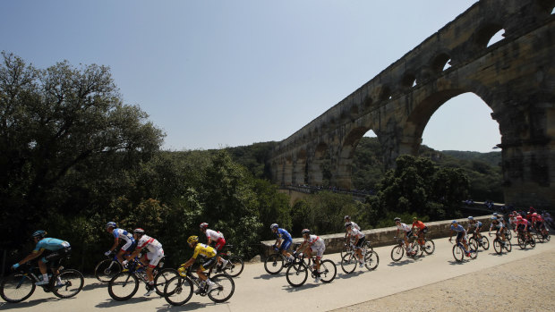 Julian Alaphilippe, wearing the overall leader's yellow jersey, rides with the pack next to the Pont du Gard.