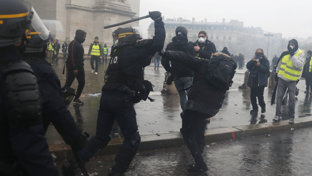 A riot police officer uses his baton on a demonstrator during a demonstration at the Arc de Triomphe.