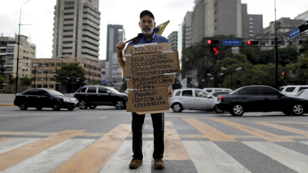 A lone protester holds a sign that reads in Spanish: "To have water, light, peace, education, work, food, medicine, transport, security, freedom: free elections, get Maduro out! Stop the usurpation!" in Caracas, Venezuela, on Thursday.