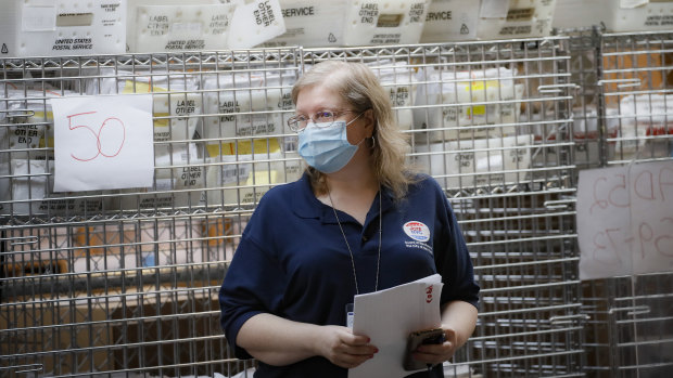 Cages loaded with ballots in postal service bins rest behind a worker at a Board of Elections facility in New York.