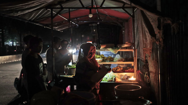 A vendor is illuminated by candle light as she serves customers at her stall during a power outage in Jakarta.