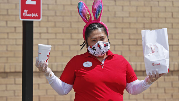 Amid COVID-19 concerns, fast food worker Silay Penalosa wears a mask and Easter bunny ears as she carries an order to a customer waiting outside a Chick-fil-A restaurant in Dallas.