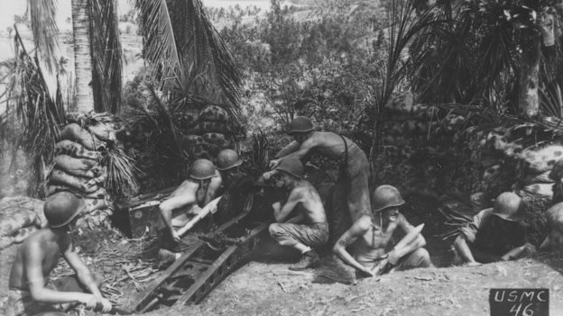 Camouflaged by the jungle and protected by sand bags, a Marine crew loads ammunition in the Solomon Islands, 1942.