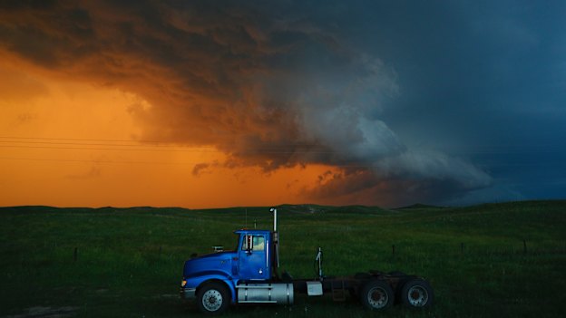A truck travels on as storms colour the background.