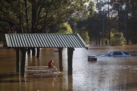 North Richmond. A young boy sits with his phone in a submerged picnic area with a stranded car in the background. 