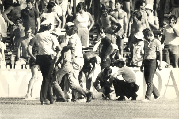 In the general melee on the field a policeman lies injured while a possible assailant is marched off.