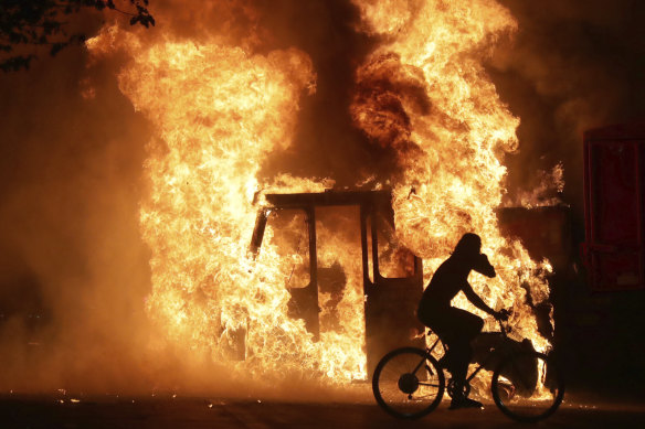 A man on a bike rides past a city truck as it burns outside the Kenosha County Courthouse. 