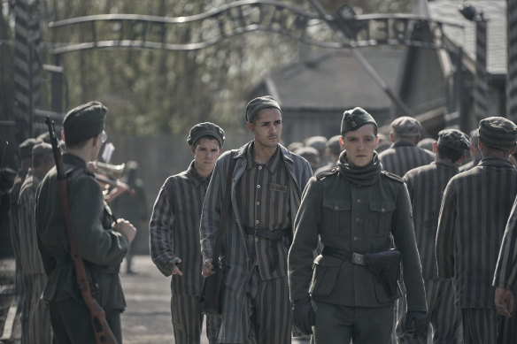 Lali (Jonah Hauer-King) walks behind Nazi officer Stefan Baretzki (Jonas Nay) in The Tattooist of Auschwitz.