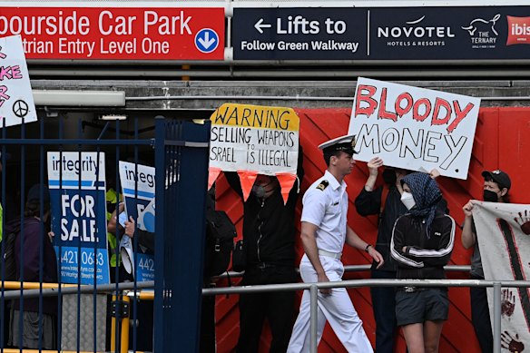 A defence person walks past people protesting at Tumbalong Park near the Indo-Pacific 2025 International Maritime Exposition held at the International Convention Centre in Darling Park, NSW.