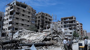People stand in front of damaged buildings, in the town of Douma, a week after the April 2018 attack.