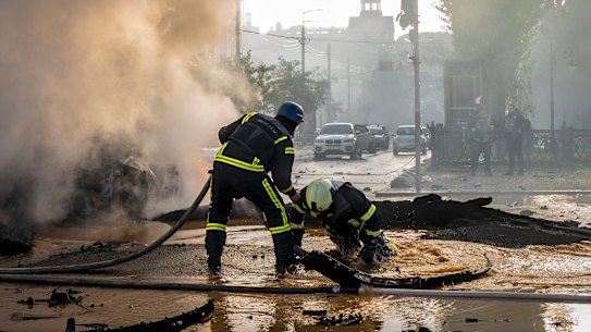 A firefighter helps his colleague  escape from a crater as they extinguish smoke from a burned car after a Russian attack in Kyiv.