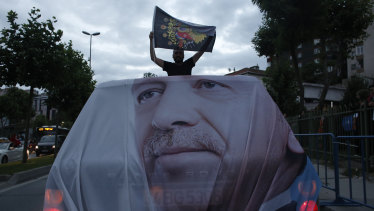 A man holds a flag while travelling in a vehicle adorned with the image of Recep Tayyip Erdogan.
