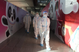 Workers wearing protective gear walk through the airport ahead of the 2022 Winter Olympics.