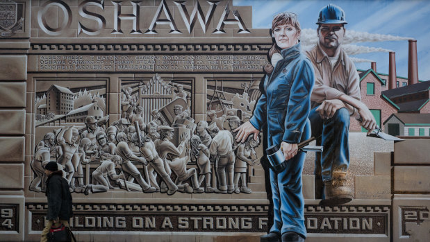 A pedestrian walks past a mural depicting workers in Oshawa, Ontario, Canada. After churning out cars and trucks for General Motors for more than a century, the town could find itself without a car plant.